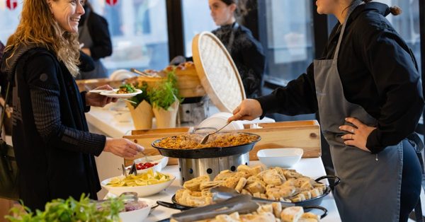 Medewerker schept eten op bij een lunchbuffet waar een klant met een bord in de hand vriendelijk toekijkt