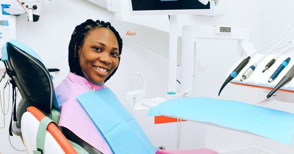 Une femme souriante assise dans le fauteuil d'un cabinet dentaire moderne avec du matériel médical en arrière-plan