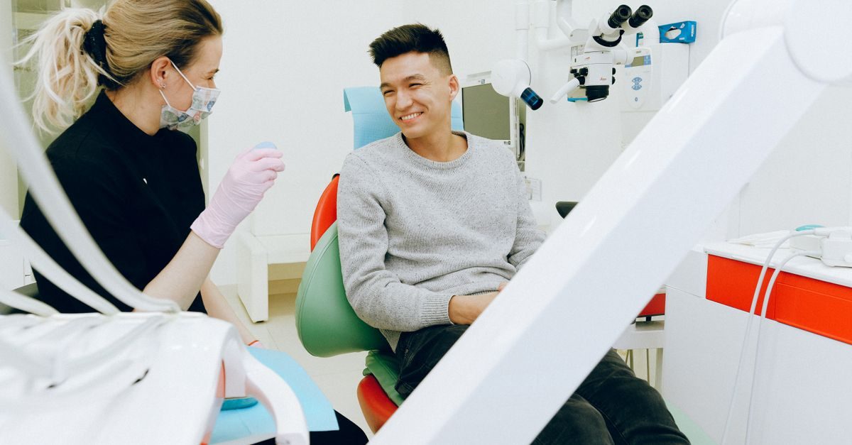 Dentista con mascherina parla sorridendo con un paziente seduto sulla poltrona in uno studio moderno e luminoso