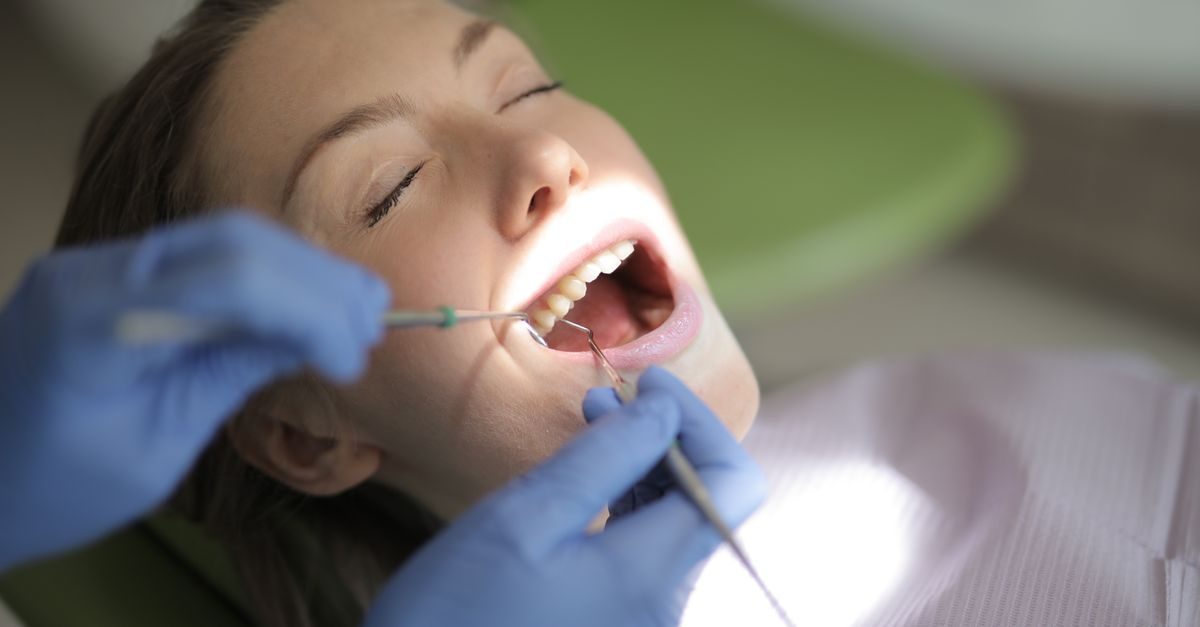 Dentysta w niebieskich rękawiczkach bada zęby spokojnej pacjentki w gabinecie stomatologicznym
