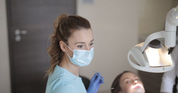 Tandarts met mondmasker en blauwe handschoenen behandelt een patiënt in een verlichte tandartspraktijk