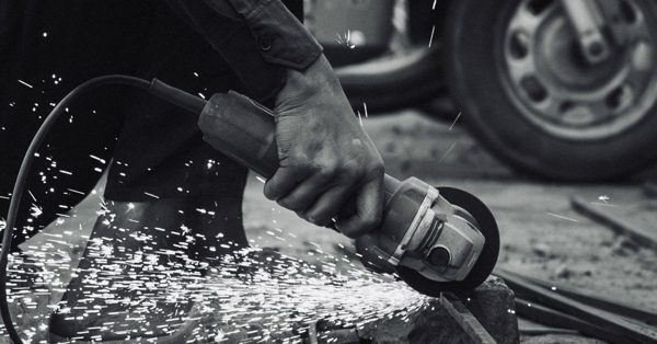 Hand die met een haakse slijper metaal bewerkt waarbij vonken in het rond vliegen in een zwart-wit setting