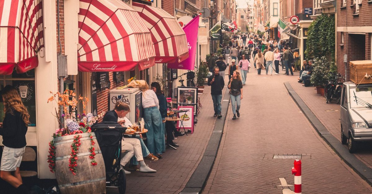 Mensen wandelen en zitten op een terras in een drukke, gezellige winkelstraat in een Nederlandse stad