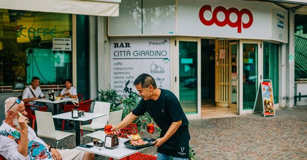 Ober serveert drankjes en hapjes op het terras van Bar Città Giardino voor een Coop-supermarkt