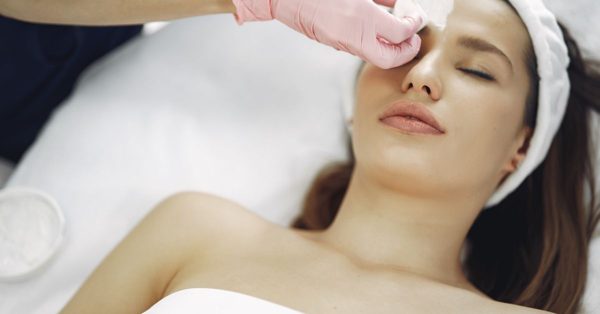 Une esthéticienne en gants roses applique un soin sur le visage d'une cliente détendue dans un institut de beauté