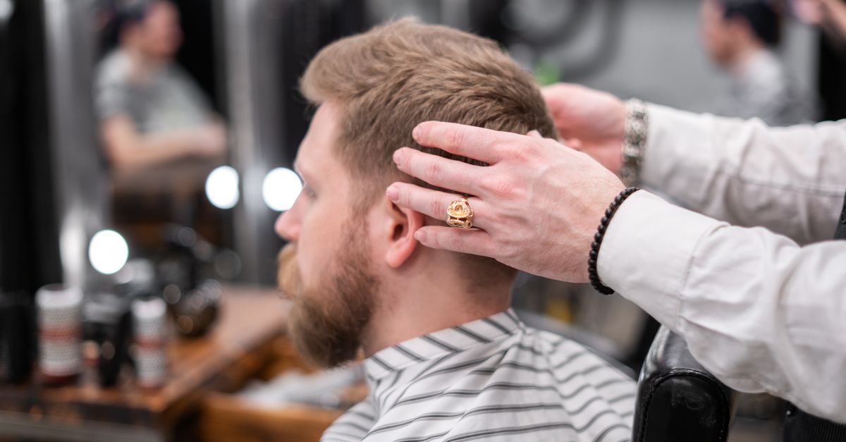 Parrucchiere con camicia bianca sistema i capelli a un cliente con barba in un salone professionale moderno