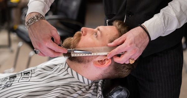Frisör klipper skägg på en kund i en professionell barberarsalong med fokus på precision och hantverk