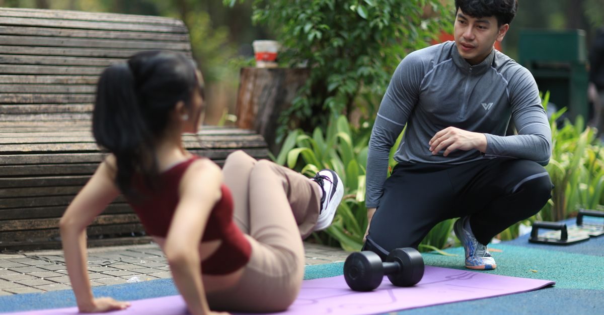 Un coach sportif conseille une femme faisant des exercices abdominaux sur un tapis de yoga dans un parc
