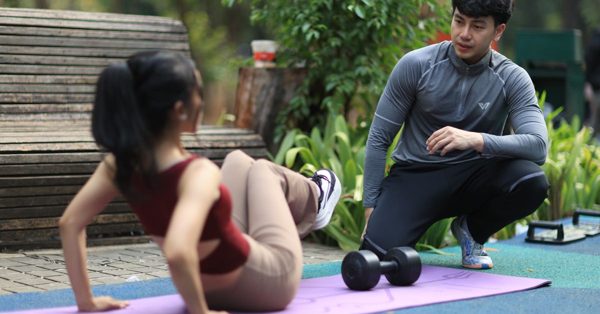 Un coach sportif conseille une femme faisant des exercices abdominaux sur un tapis de yoga dans un parc