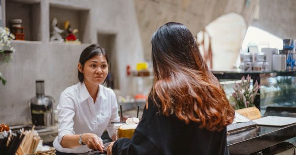 Een medewerkster in een wit overhemd helpt een klant aan de balie van een sfeervol café