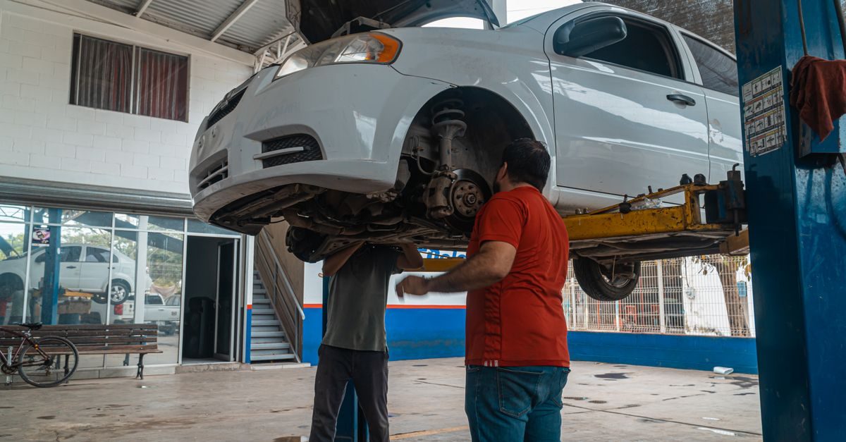 Dos mecánicos trabajan sobre un auto blanco elevado en un taller automotriz con ambiente profesional y enfocado