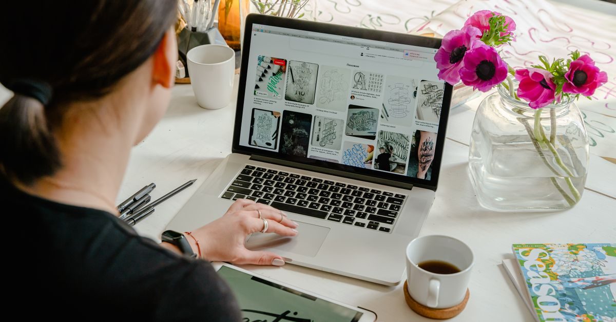 Persoon werkt achter laptop aan een bureau met koffie en bloemen in een lichte werkomgeving