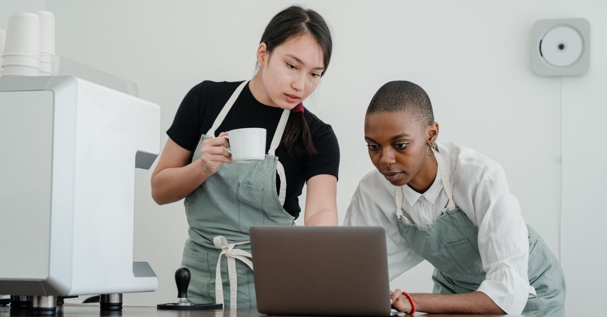 Twee baristas in schorten kijken geconcentreerd naar een laptop in een koffiebar
