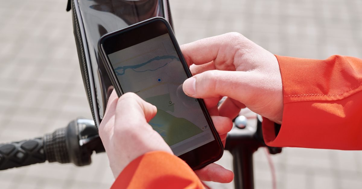 Persona con chaqueta naranja usa un teléfono móvil con un mapa digital mientras conduce una bicicleta en la calle