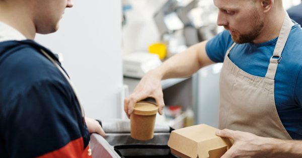 A focused cafe worker in an apron packs food into a delivery bag for a customer in a professional kitchen setting