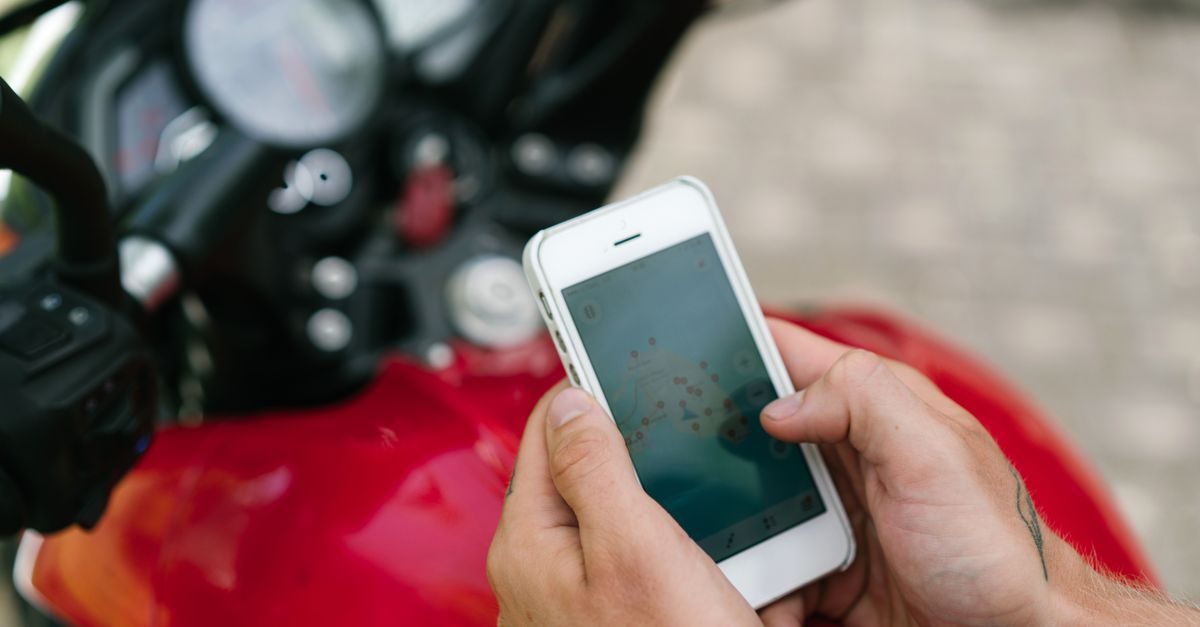 Persona usando un teléfono móvil con un mapa digital frente a una motocicleta roja estacionada