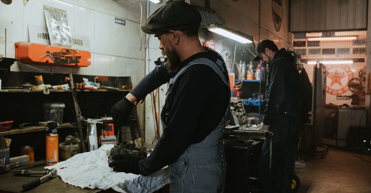 Dos mecánicos trabajan concentrados en un taller con herramientas y piezas de motor sobre una mesa de trabajo