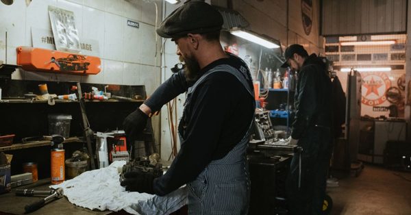 Dos mecánicos trabajan concentrados en un taller con herramientas y piezas de motor sobre una mesa de trabajo