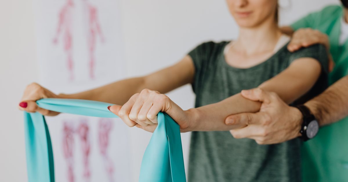 Physiotherapeut unterstützt eine Patientin bei Übungen mit einem hellblauen Widerstandsband in einer Praxis