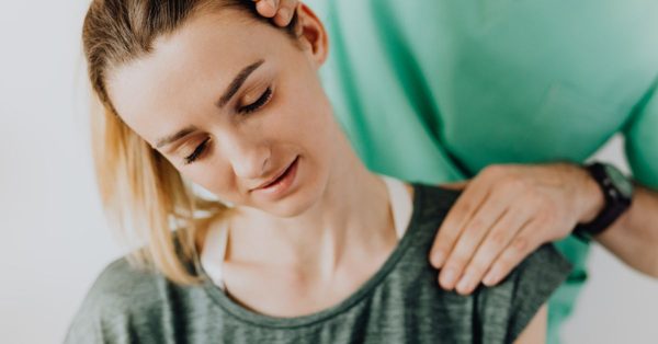 Fysiotherapeut in groen uniform masseert de nek en schouders van een ontspannen vrouw
