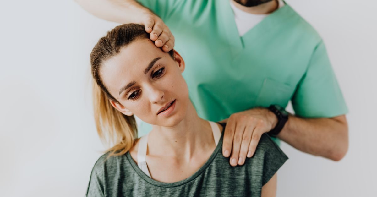 Fisioterapeuta con uniforme verde ajusta el cuello de una paciente que muestra una expresión de molestia física
