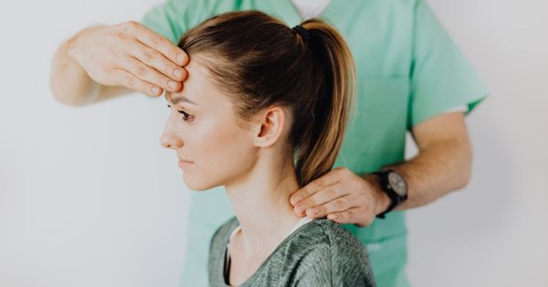 Fisioterapeuta con uniforme verde examina la cabeza y el cuello de una paciente en un entorno clínico profesional