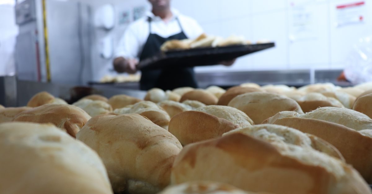 Bakker in wit uniform met zwart schort houdt een bakplaat met versgebakken broodjes vast in een professionele bakkerij