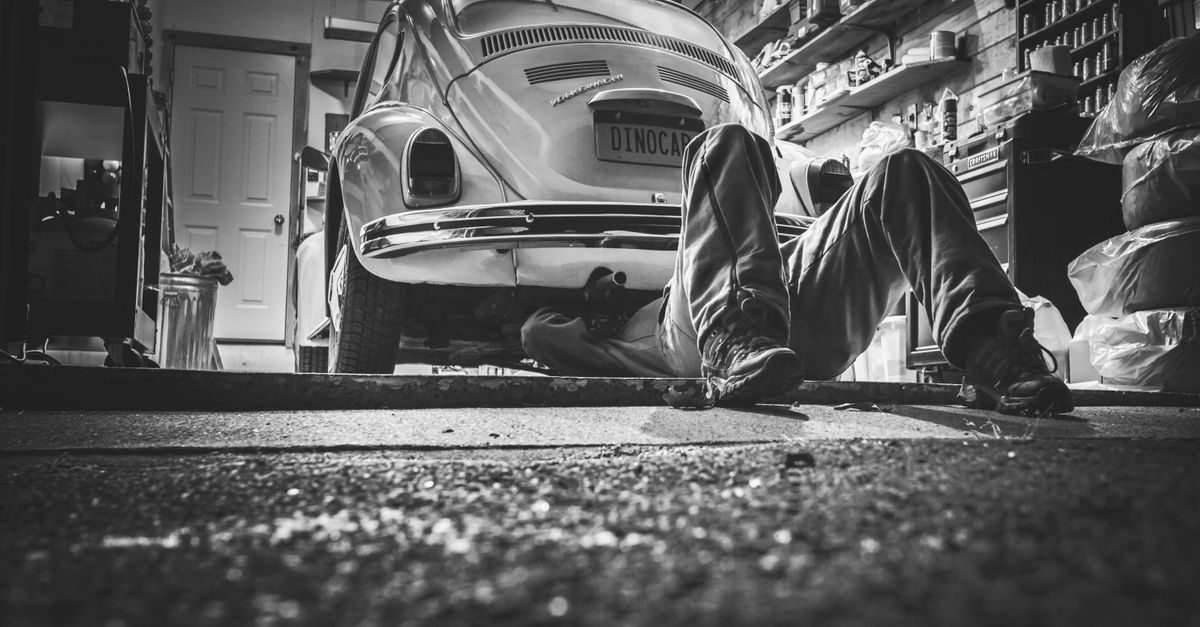 Meccanico sdraiato sotto una Volkswagen Maggiolino in un'officina disordinata durante un intervento di riparazione