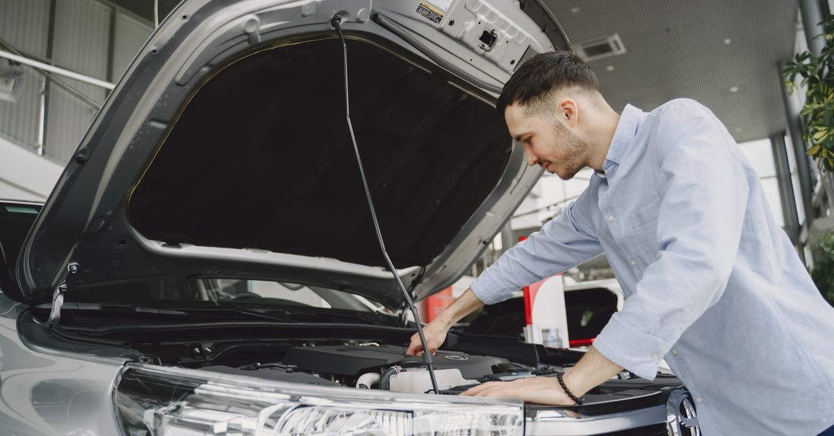 Un joven técnico revisa concentrado el motor de un coche con el capó abierto en un taller profesional