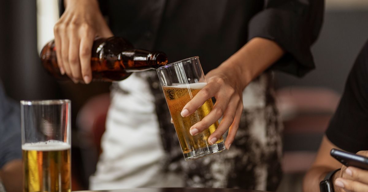 Persoon schenkt bier uit een fles in een glas in een informele setting met een ander glas en een smartphone op tafel