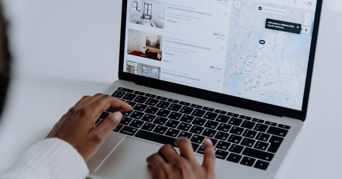 Mains d'une personne utilisant un ordinateur portable pour rechercher des logements sur une carte interactive en ligne