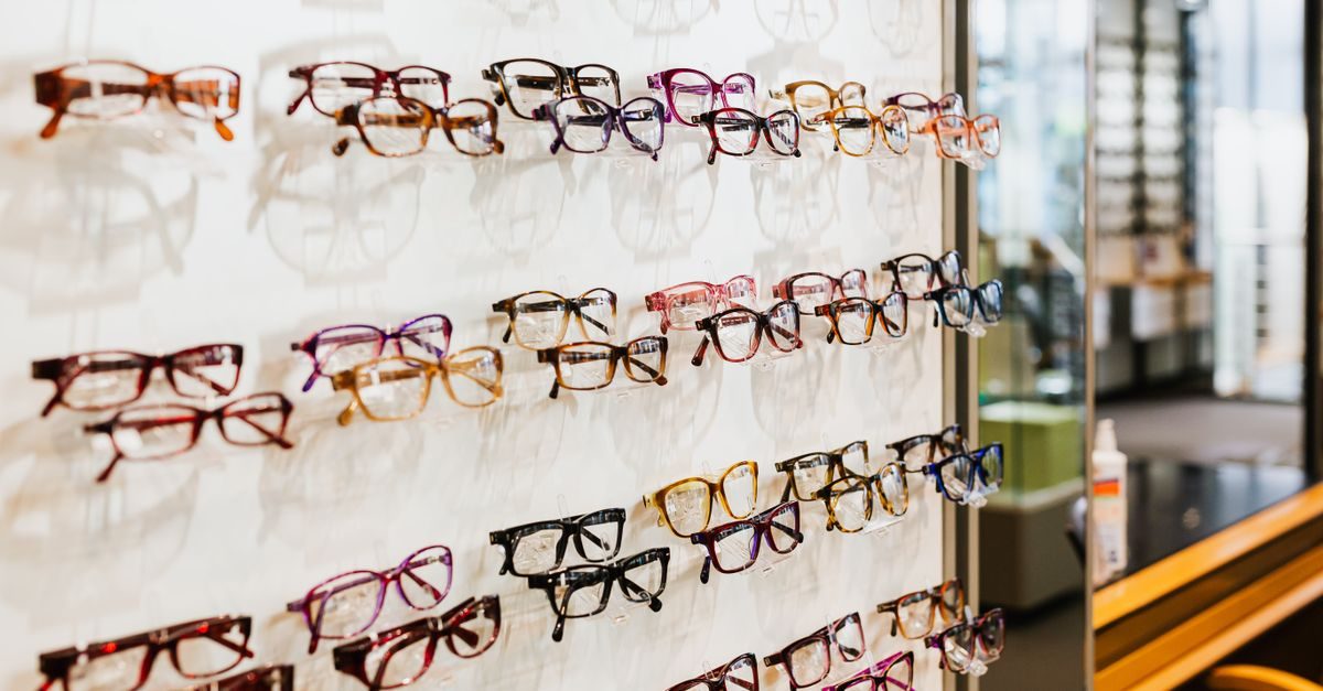Exhibición de diversas gafas graduadas de colores y estilos variados expuestas en una pared blanca de una óptica
