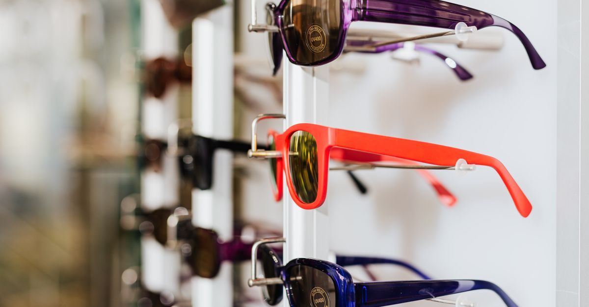 Mehrere bunte Sonnenbrillen hängen in einer hellen Auslage an einer weißen Wand in einem Optikergeschäft