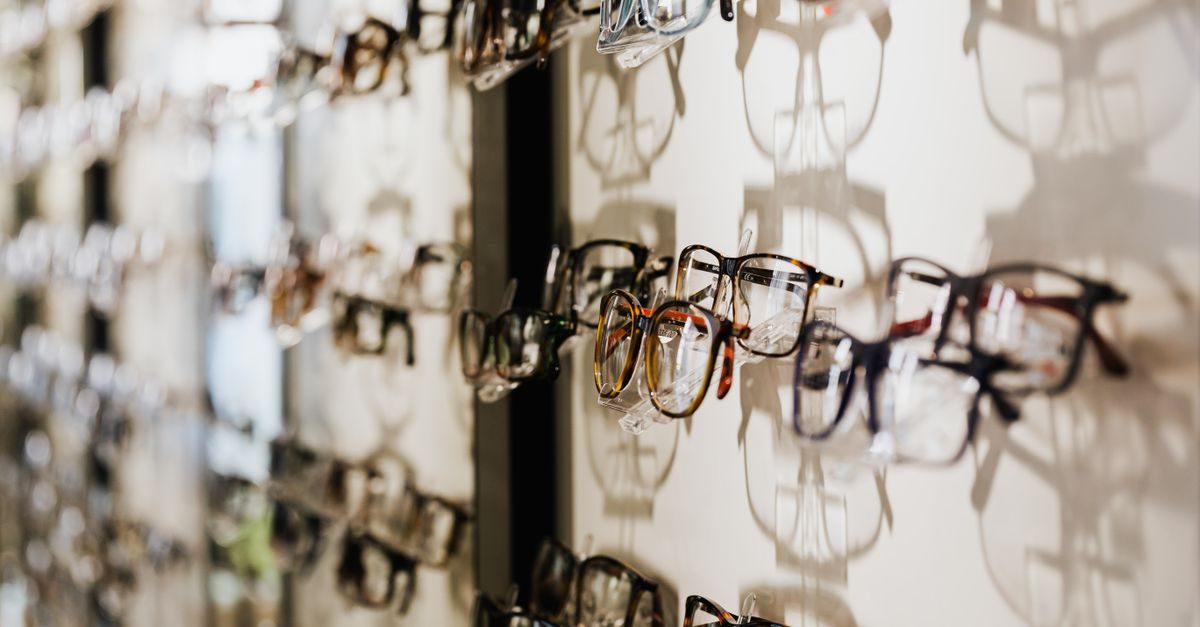 Rows of various eyeglass frames displayed on a bright wall in an optician shop with soft shadows cast behind them