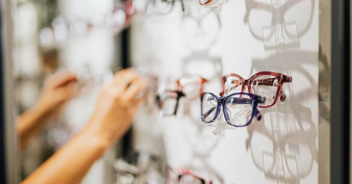 Mani che scelgono occhiali da vista esposti su una parete in un negozio di ottica con illuminazione soffusa