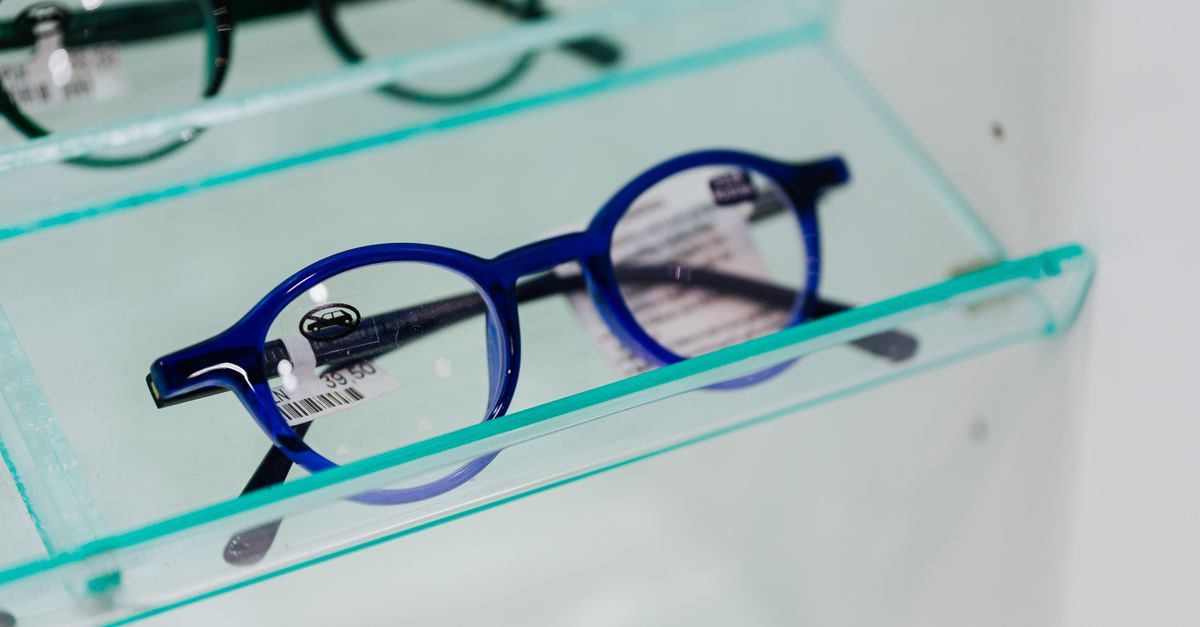 Blå runda glasögonbågar med prislapp ligger på en glashylla i en optikerbutik