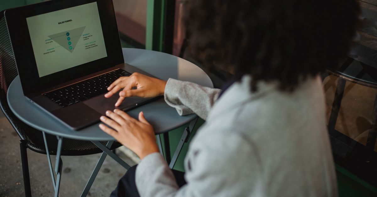 Persona con capelli ricci lavora al computer portatile su un tavolino rotondo analizzando un grafico di funnel di vendita