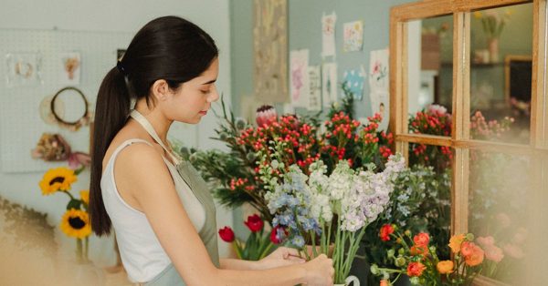 Eine Floristin mit Pferdeschwanz bindet in ihrem hellen Blumenladen konzentriert einen Strauß aus bunten Blumen