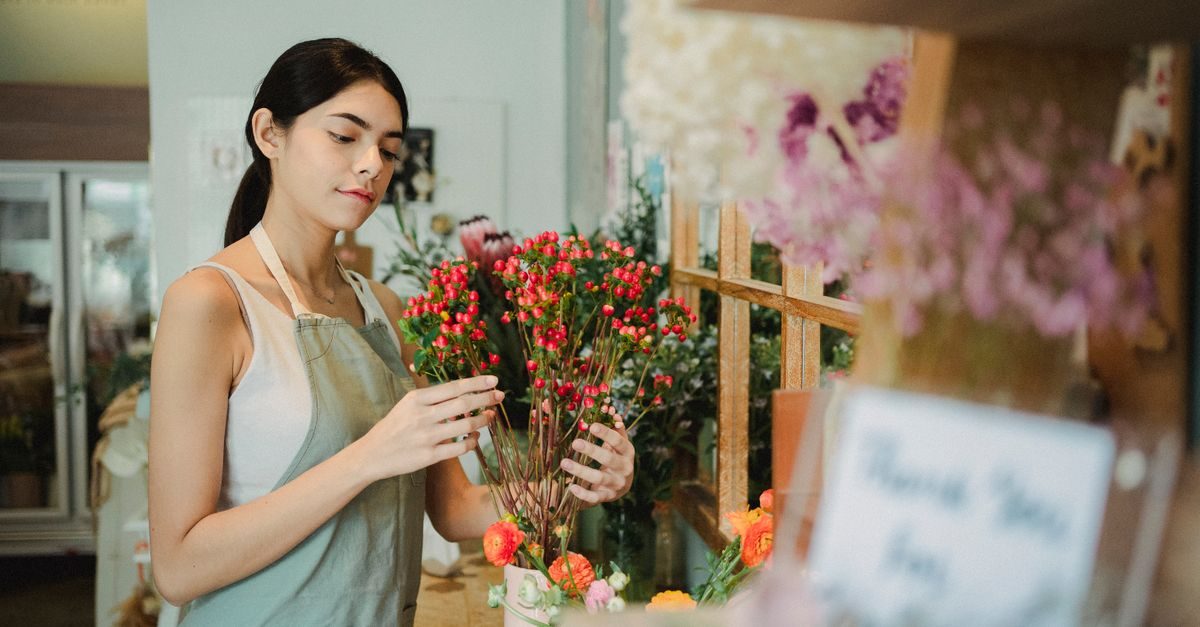Geconcentreerde bloemist in een schort schikt rode bessen en bloemen in een sfeervolle winkel