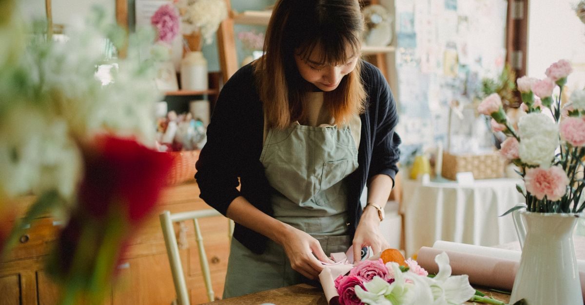 Florista concentrada envuelve un ramo de flores frescas en una acogedora tienda con ambiente tranquilo y artesanal