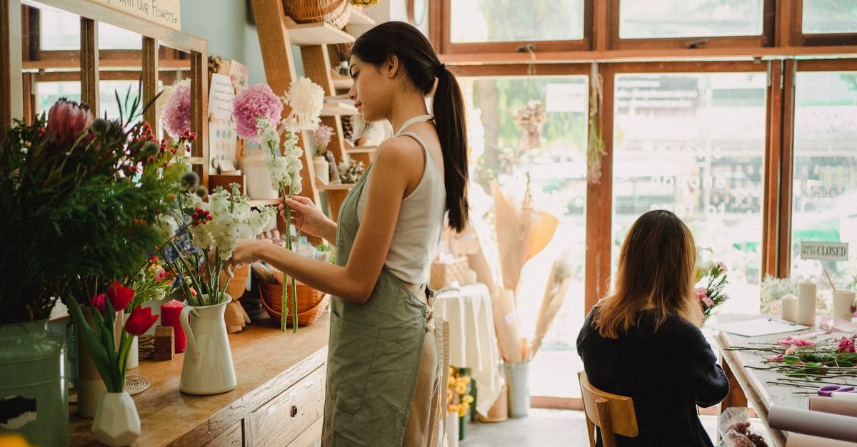 Bloemist in een sfeervolle winkel schikt bloemen in een vaas terwijl een collega aan een tafel werkt