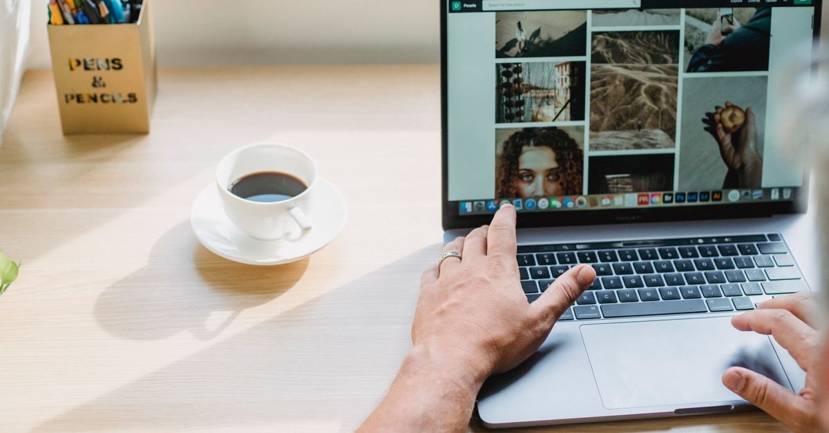 Person arbeitet an einem Laptop auf einem Schreibtisch neben einer Tasse Kaffee und einem Stiftehalter