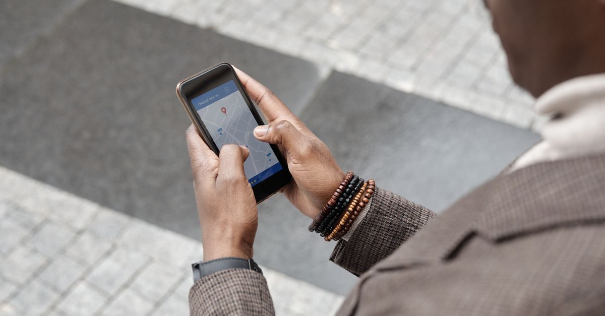 Person mit Armbändern nutzt auf einem Smartphone eine Karten-App zur Navigation auf einem gepflasterten Gehweg