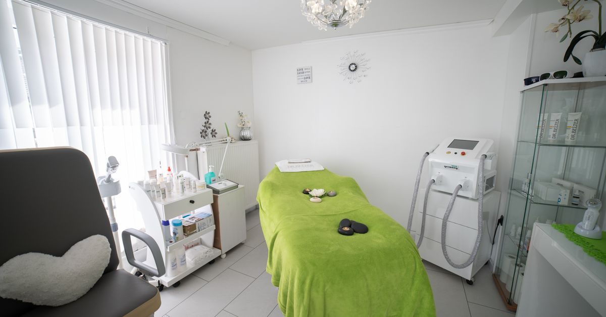 Habitación luminosa de centro de estética con camilla cubierta por una manta verde, carrito con productos y equipo médico