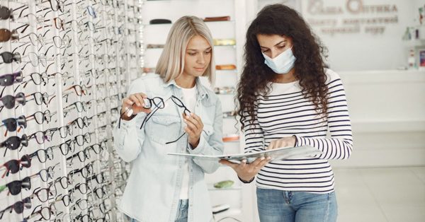 Optiker hjälper en kund att välja glasögon i en butik med väggar fyllda av bågar