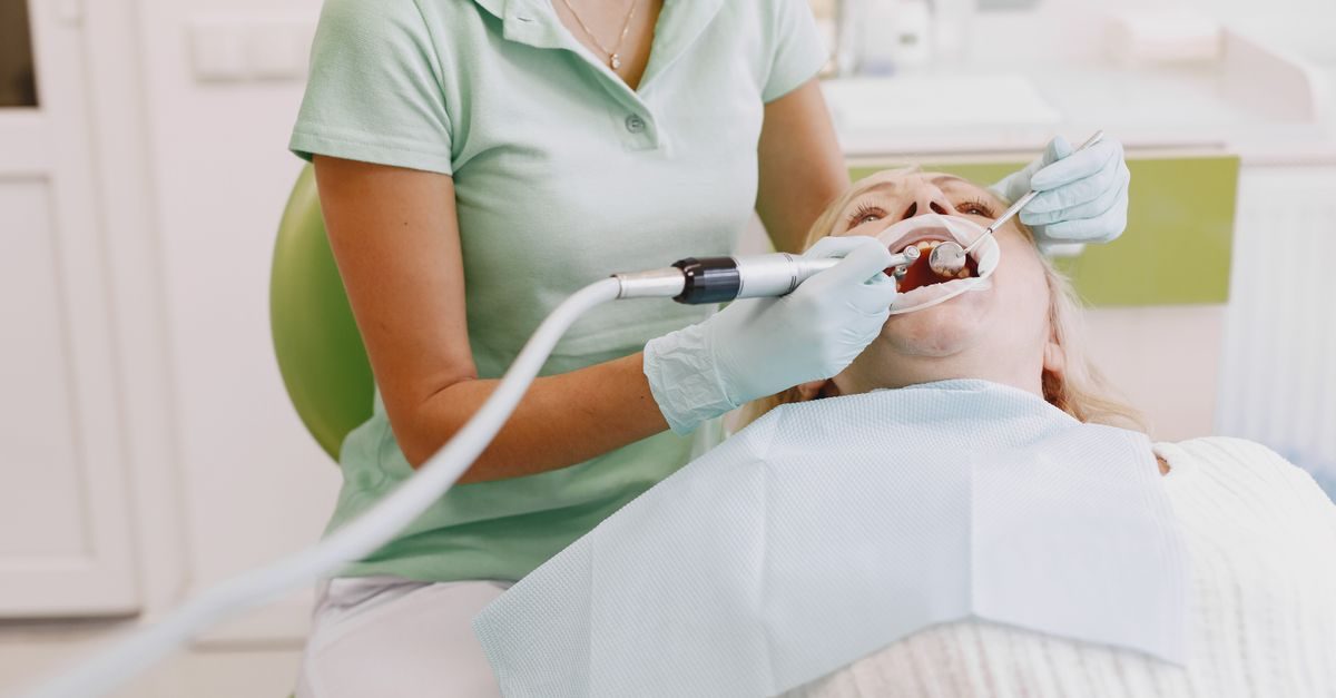 Dentista con guanti e divisa verde esegue un controllo odontoiatrico su una paziente sdraiata sulla poltrona dello studio