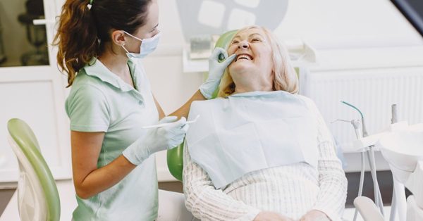 Une dentiste masquée examine les dents d'une patiente âgée souriante dans un cabinet médical lumineux