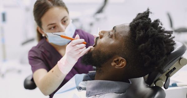 Une dentiste en tenue médicale examine les dents d'un patient allongé sur un fauteuil dans un cabinet dentaire moderne
