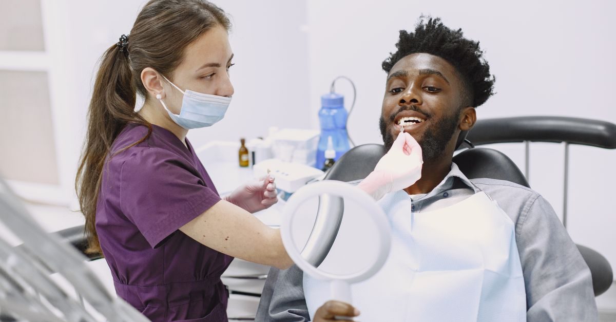 Dentista con mascherina visita un paziente sorridente seduto sulla poltrona dello studio odontoiatrico