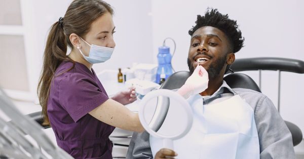 Dentista con mascherina visita un paziente sorridente seduto sulla poltrona dello studio odontoiatrico